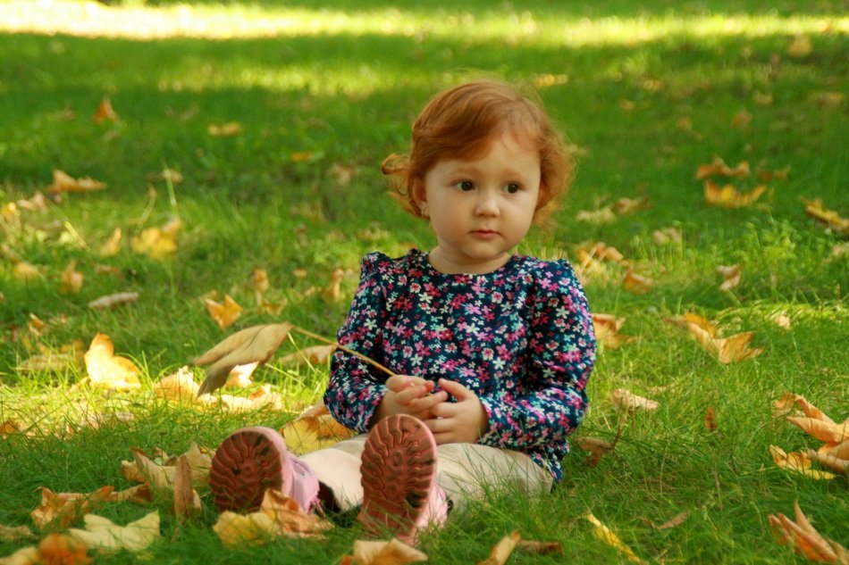 baby girl sitting with yellow leaf in hand