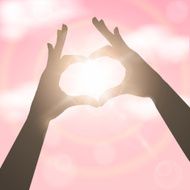 Hands in the form of heart over pink sky