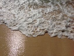 Sand covered with water and foam on the Pacific coast of the island of Saipan