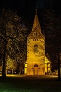 Illuminated church with a spire at night among trees