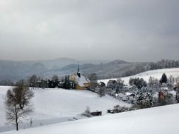 distant view of a church amid a snowy landscape in hinterhermsdorf
