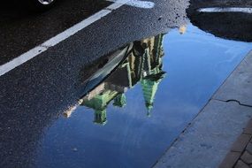 church mirroring on puddle on road, amsterdam