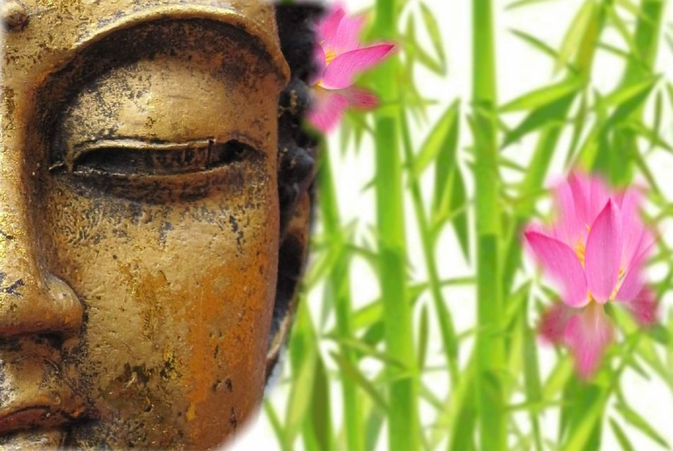 Buddha head on a background of a green plant with flowers