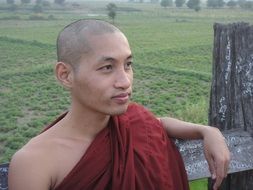 buddhist monk sits near wooden fence