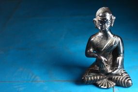 silver figurine of a buddha on a blue background