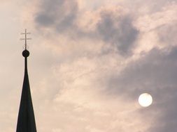 spire with a cross on a cloudy sky background