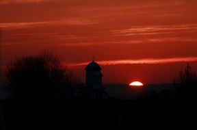 red sun sky over black silhouettes of church