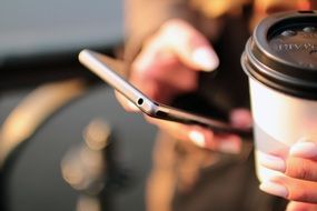 smartphone and cup coffee in hands