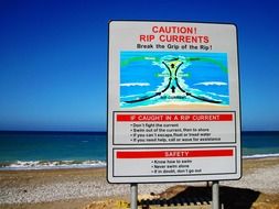 rip currents, caution sign on beach at water