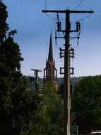 steeple among power piles and tree tops