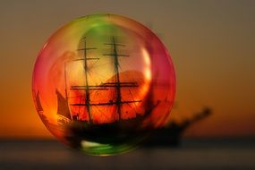 view of sailing ship on sea at sunset through soap bubble