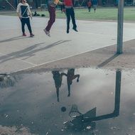 reflection of kids playing basketball on puddle