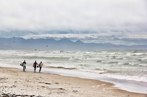 three surfers on a beach in south africa