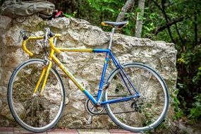 yellow-blue bike is parked by the stone