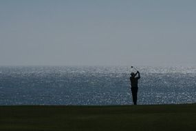 silhouette of a golfer on the coast at sunset