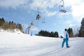 snowboarders on ski lift above snowy mountain side