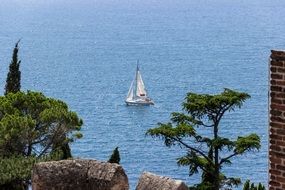 sailing boat on the water behind rocks and green trees