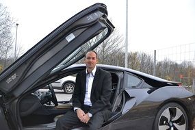 A man is sitting near a luxury car