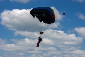 The paratrooper is hovering against the cloudy sky