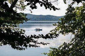 canoe with people on the lake behind the branches