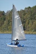 man in sailing boat in view of forested bank