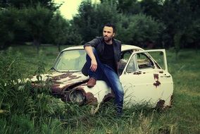 a man posing on an old rusty car