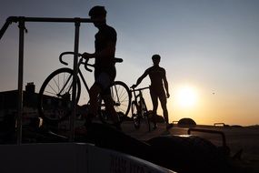 silhouettes of two cyclists in helmets at sunset sky