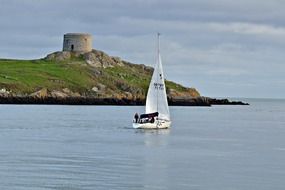 sailing boat on sea in view of ancient tower on island