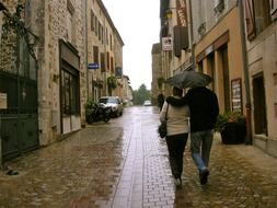 Couple walking with umbrella on the wet street among buildings