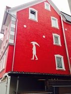 man with umbrella, white mural at red house wall