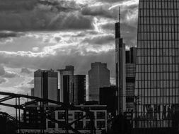 black and white photo of skyscrapers, bridge and clouds