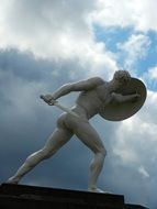 Sculpture of a man with a sword and shield against a cloudy sky background