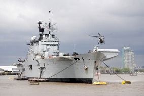 helicopter above aircraft carrier lying at anchors on thames river, uk