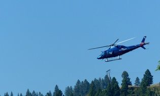 Helicopter flying over the forest at blue sky background