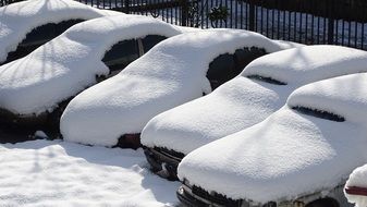 row of cars covered with snow at fence