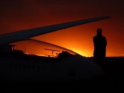 orange sunset and silhouette of a man and plane wing