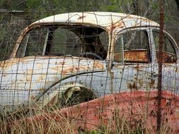ruined vintage car behind wire fence