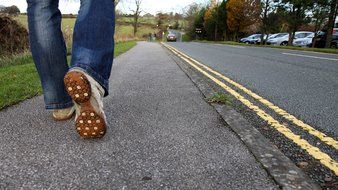 male legs in sports shoes walking on sidewalk at road