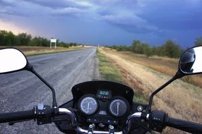motorcycle steering wheel in view of road under stormy sky
