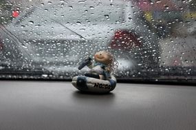 Car window with the raindrops above the colorful cute doll inside the car