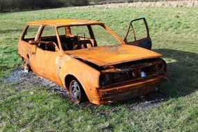 burnt car on green grass on a sunny day