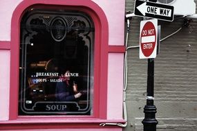 post with traffic signs at pink window of restaurant