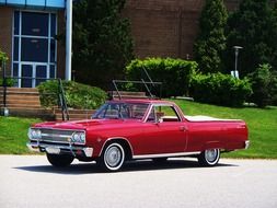 red chevrolet stands on the road near a green meadow