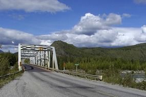 metal bridge over the river against the backdrop of the green mountains