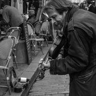 black and white photo of a street musician in paris with a guitar