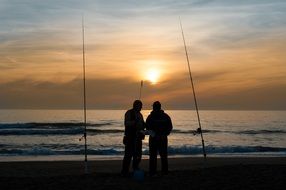 fishermen with fishing rods on the beach at sunrise