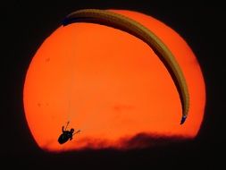 man on paraglider on orange sun background