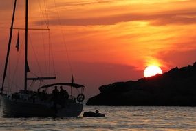 sailing boat on sea near coast at sunset
