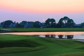 green golf course with a pond against the evening sky