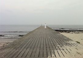 a man in white clothes walks along the boardwalk at the beach